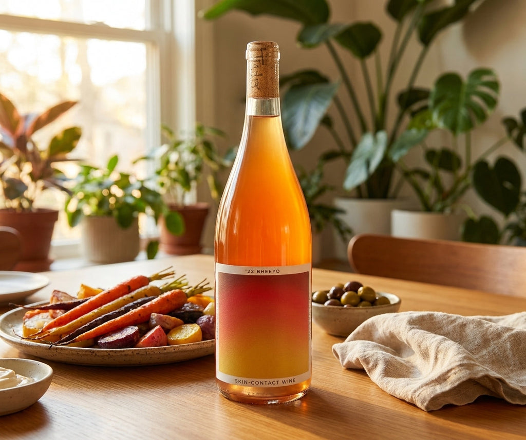 Bheeyo skin-contact orange wine bottle on a vegan dinner table with roasted vegetables