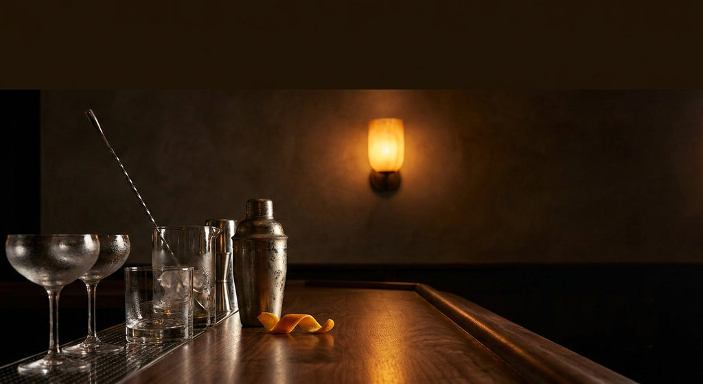 Craft cocktail bar counter with coupe glasses, shaker and orange peel at dusk