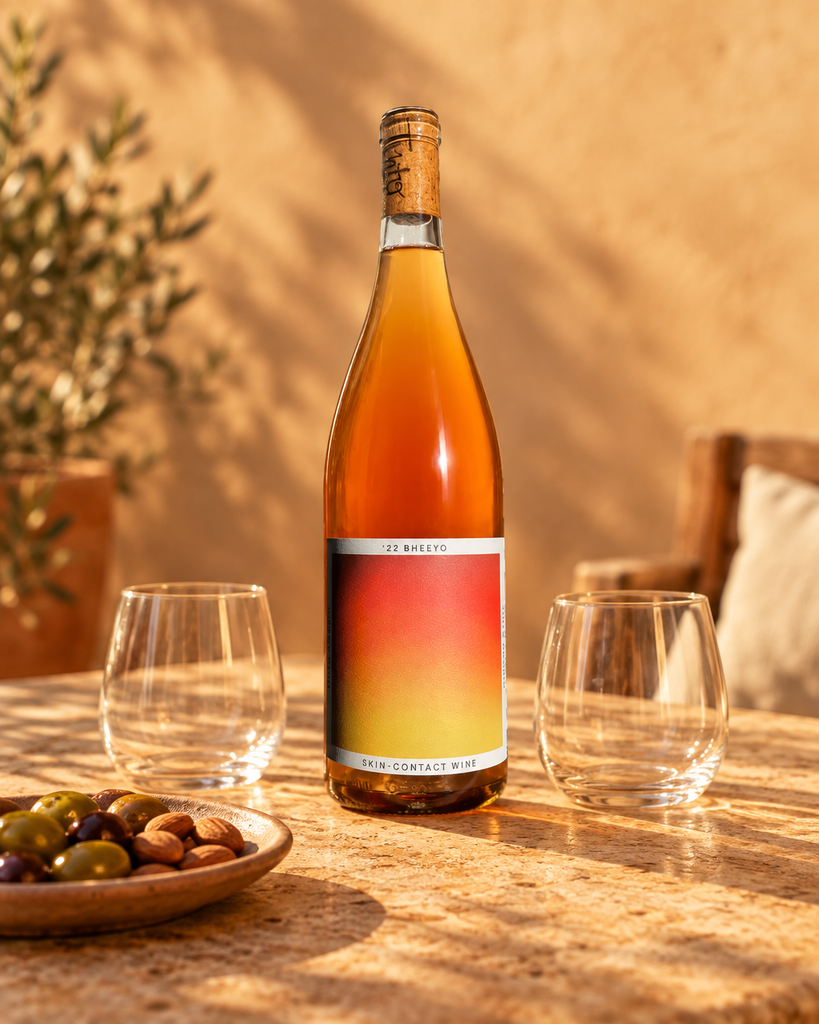 '22 Bheeyo skin-contact orange wine bottle on a sunlit patio table with olives and two glasses at golden hour