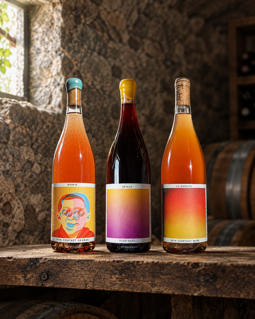 Tinto Amorio Natural Wine Sampler bottles (Monje, Jajaja, '22 Bheeyo) on a wooden shelf in a stone wine cellar